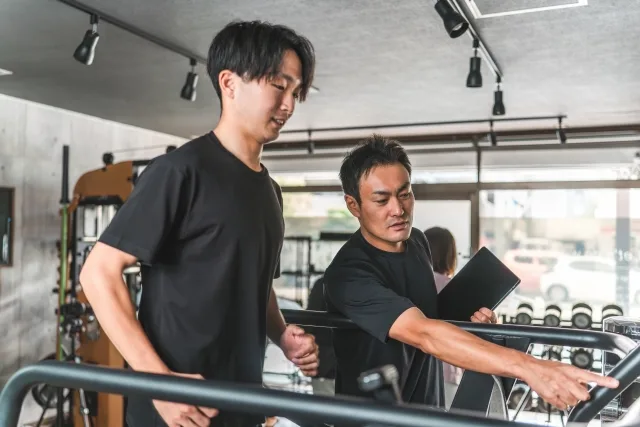 男性トレーナーにトレーニング指導を受けている男性クライアント